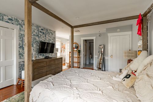 Bedroom with wood canopy bed, botanical wallpaper and a dresser-mounted TV
