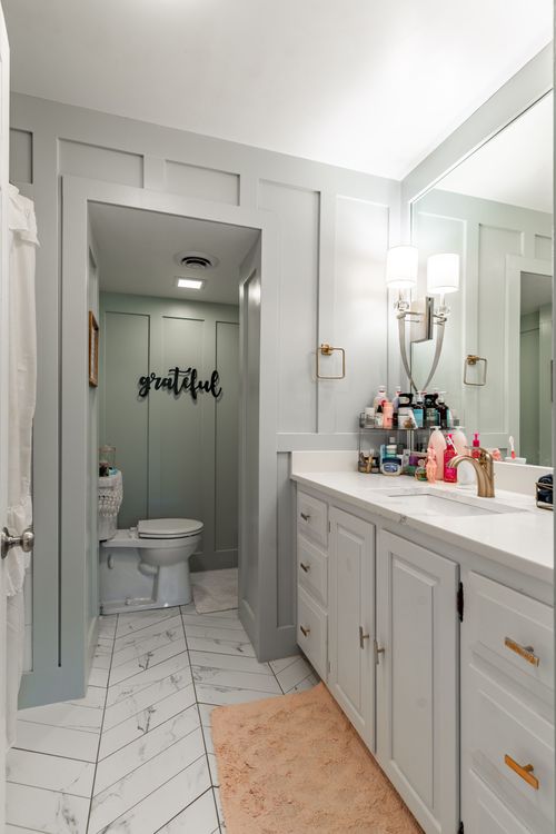 Bathroom with gray paneled walls, white vanity and herringbone tile floor