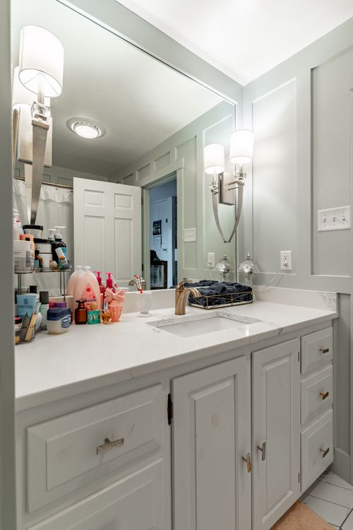 Bathroom vanity close-up with white cabinetry, sconce lighting and marble counter