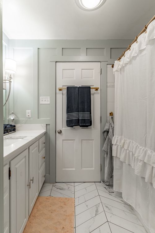 Bathroom with herringbone tile floor, navy towels and a ruffled shower curtain