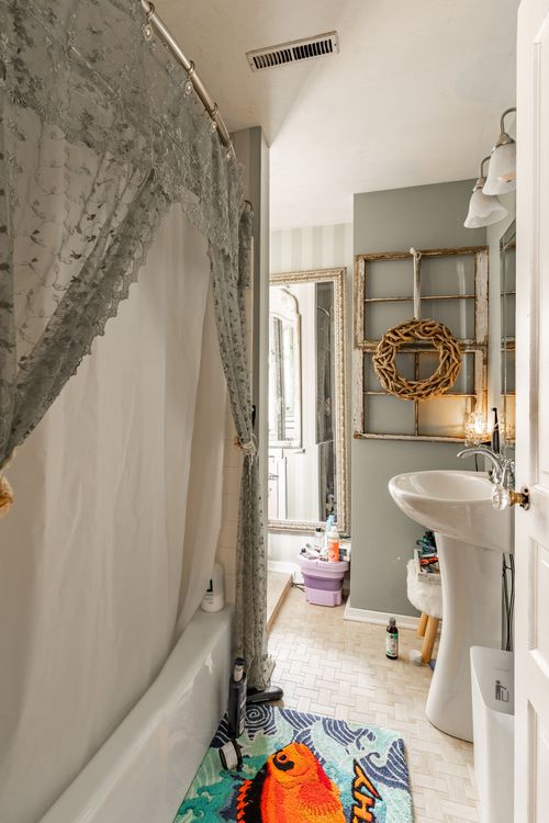 Bathroom with lace shower curtain, pedestal sink and a woven wreath accent
