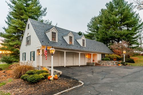 White carriage house with three garage bays, dormer windows and fall pumpkin display