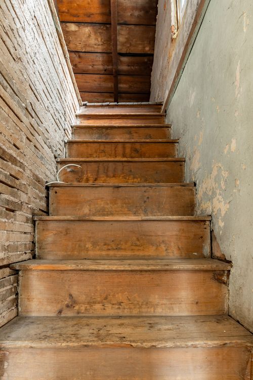 Rustic wood staircase with exposed brick wall and worn plank treads
