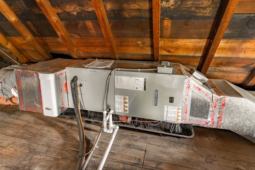Attic HVAC unit and ductwork set beneath exposed wood roof rafters