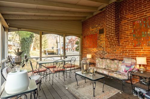 Screened porch with wrought iron furniture, floral cushions and a brick wall