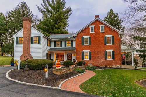 Brick and white clapboard farmhouse exterior with chimney and autumn landscaping