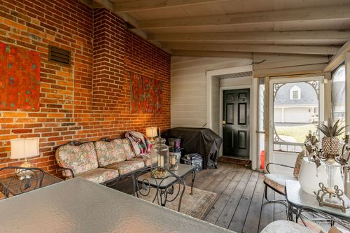Screened porch with exposed brick wall, colorful art and wicker seating