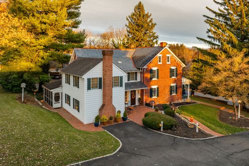 Aerial view of a brick and white clapboard farmhouse framed by fall trees