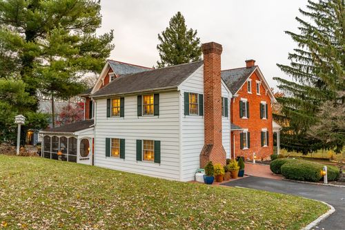 Elevated view of a brick and white farmhouse with tall evergreens and a paved driveway