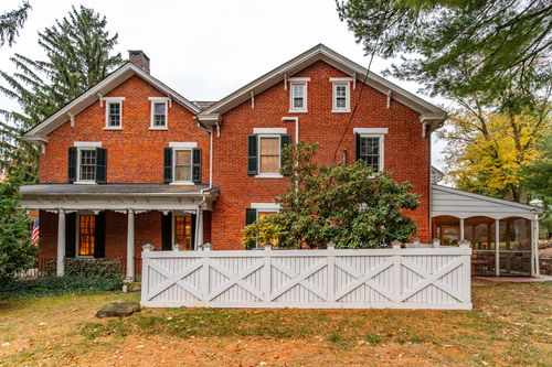 Brick farmhouse exterior with twin gables, white porch railing and fall foliage
