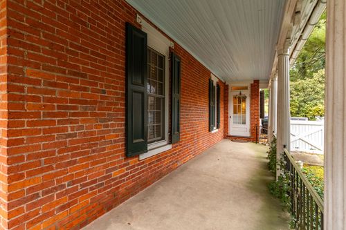 Covered brick porch with dark shuttered windows and painted wood ceiling