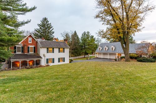 Aerial view of a brick farmhouse with white addition, attached garage and mature trees