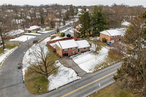 Aerial winter view of a brick ranch home along a snow-dusted suburban street
