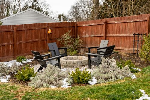 Backyard fire pit with black Adirondack chairs surrounded by winter landscaping