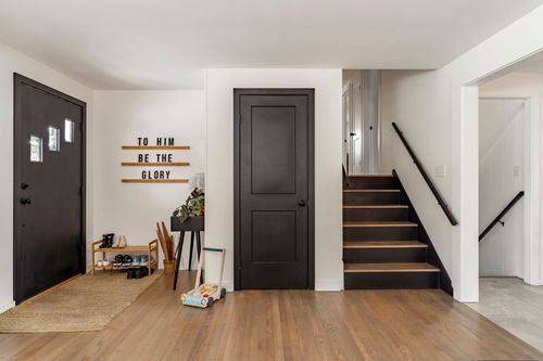 Entry sitting area with black staircase, wicker credenza and gray accent chairs