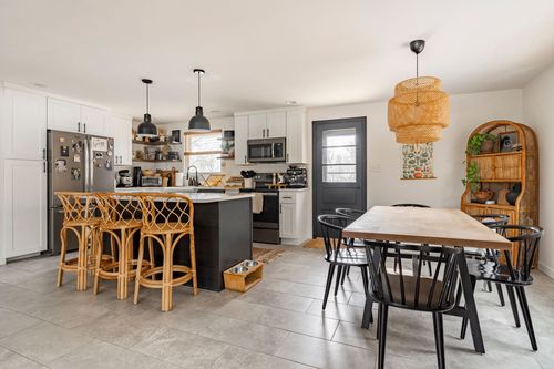Open living area with black staircase, gray accent chairs and view into the kitchen