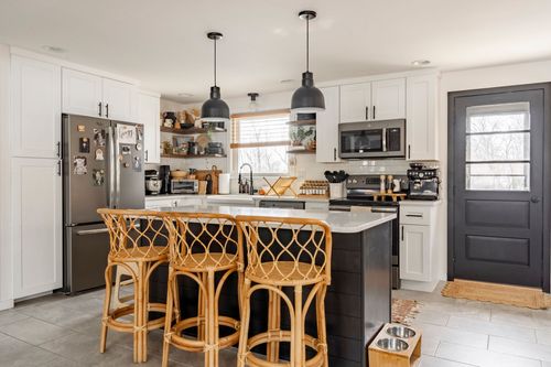 White kitchen with black island, stainless appliances and pendant lighting