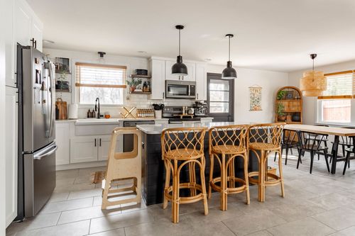 Open kitchen with stainless refrigerator, black island and rattan counter stools