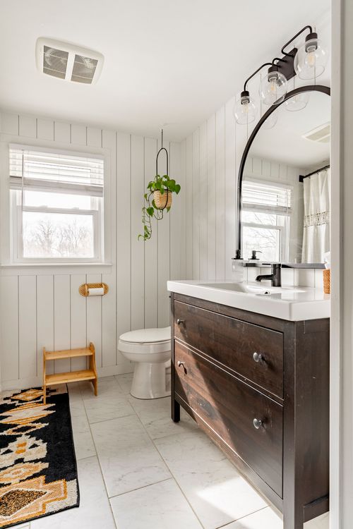 Bathroom with dark wood vanity, arched mirror and black wall sconces