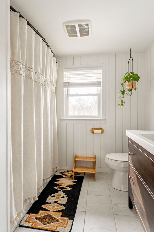 Bathroom with linen shower curtain, dark wood vanity and patterned bath mat