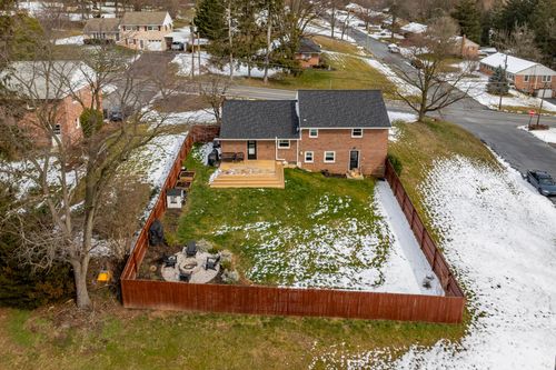 Aerial winter view of a brick home's fenced backyard with fire pit and patches of snow