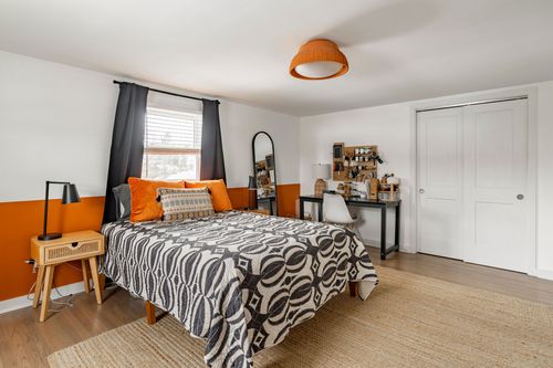 Bedroom with orange accent wall, black curtains and graphic patterned bedding