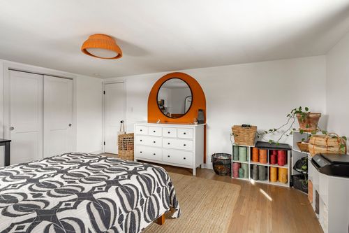 Bedroom with orange dome pendant, round mirror and white dresser