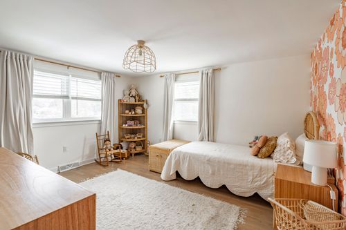 Bright bedroom with white bedding, wicker bookshelf and floral accent wall