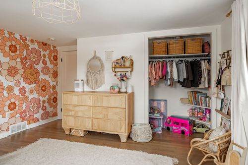 Kids bedroom with floral wallpaper, wood dresser and an organized walk-in closet