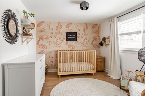 Nursery with cactus print wallpaper, wood slat crib and a round tufted rug