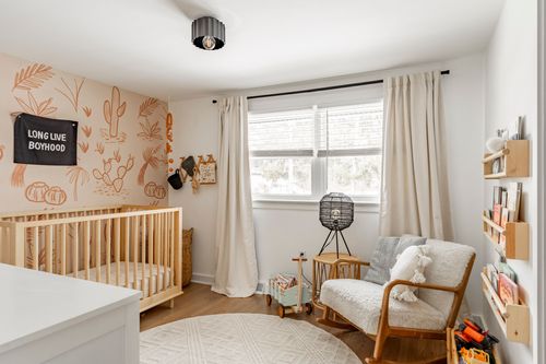 Nursery corner with a wood crib, cactus wallpaper and a wicker rocking chair