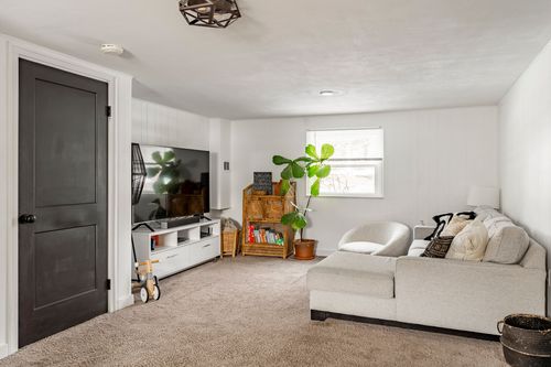 Basement family room with a gray sectional sofa, wood TV console and dark door