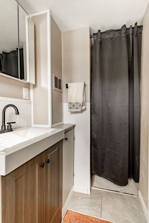 Narrow bathroom with a wood vanity, black shower curtain and marble-look tile