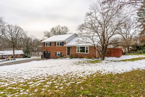 Brick split-level home with black shutters, dark garage door and snowy lawn