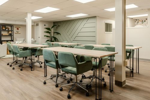 Conference room with long tables, green chairs and a sage herringbone accent wall in view