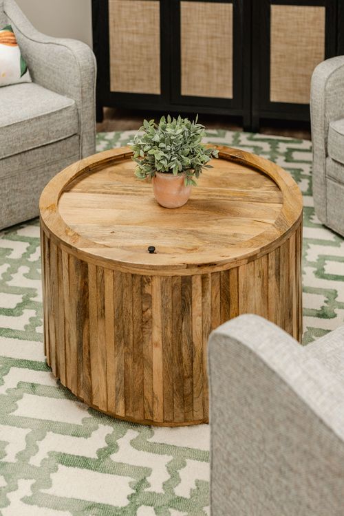 Close-up of a round wood coffee table with a potted plant between upholstered chairs