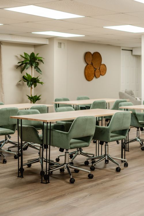 Conference room with green chairs at long tables, a round wall art medallion and houseplants