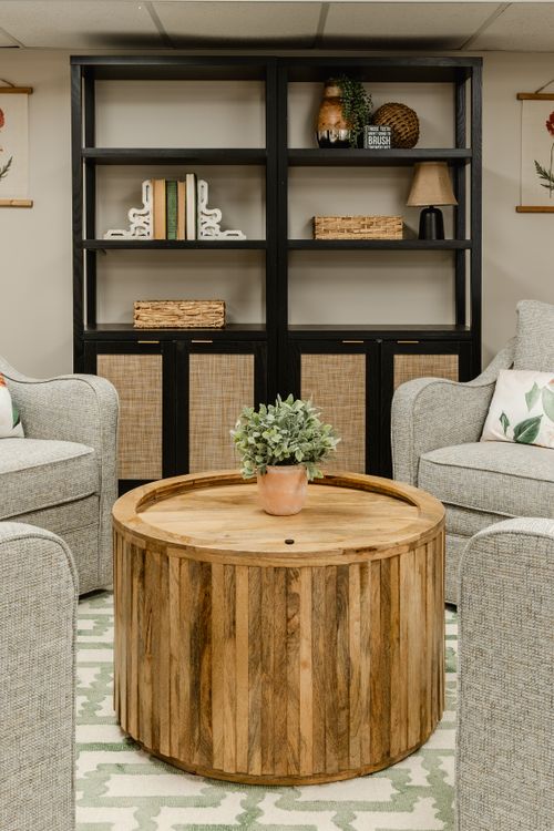 Lounge seating area with a black bookshelf, neutral chairs and a round wood coffee table