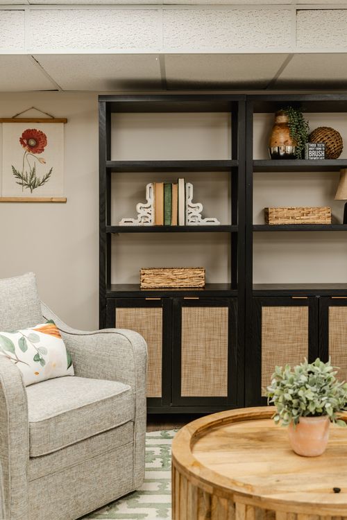 Close-up of a black bookshelf corner beside a neutral upholstered chair and botanical art