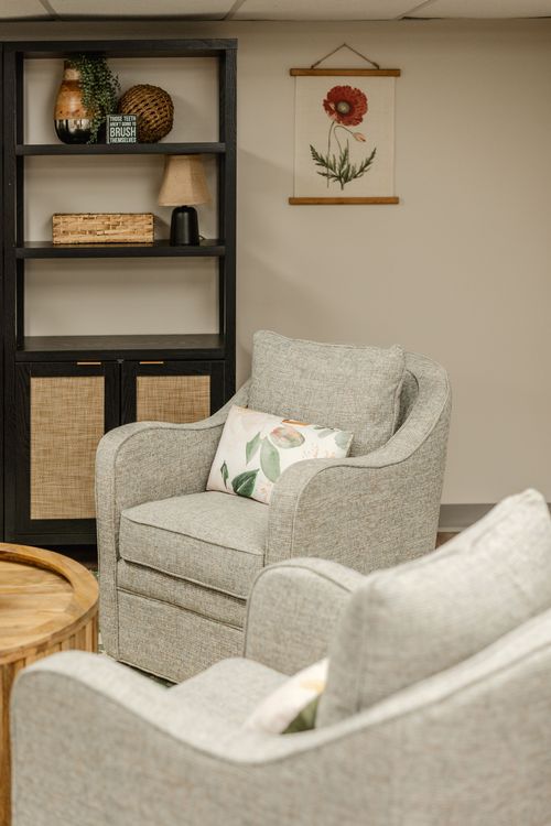 Close-up of a botanical art print beside a neutral upholstered chair with throw pillow