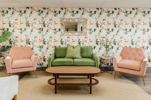 Waiting room seating with pink and green upholstered chairs against floral wallpaper