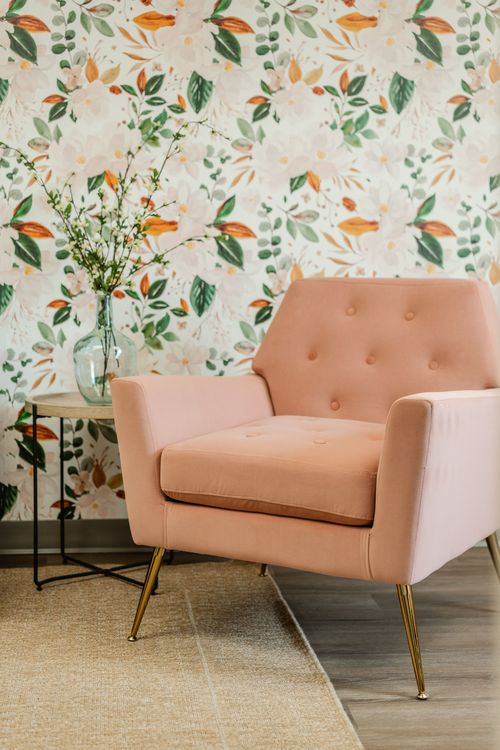 Close-up of a pink tufted armchair against botanical floral wallpaper