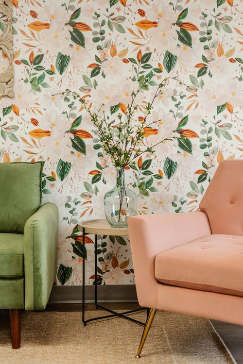 Close-up of pink and green upholstered chairs against floral wallpaper with a side table