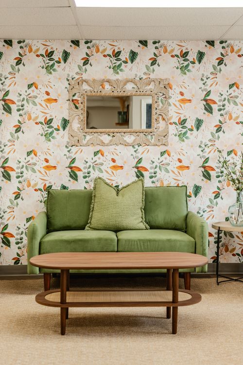 Waiting room with a green loveseat, ornate wood mirror and floral wallpaper