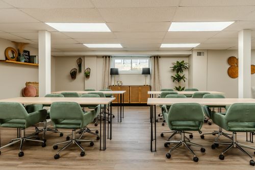 Conference room with long tables, green chairs and a window framed by sheer curtains