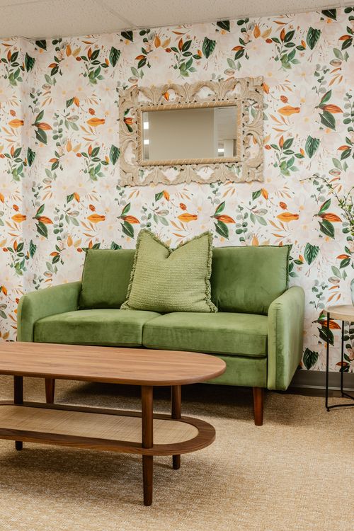 Waiting room with a green loveseat, ornate mirror and round wood coffee table
