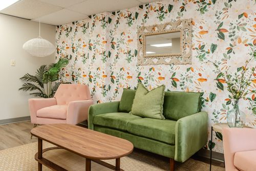 Waiting room with pink and green upholstered seating against botanical floral wallpaper