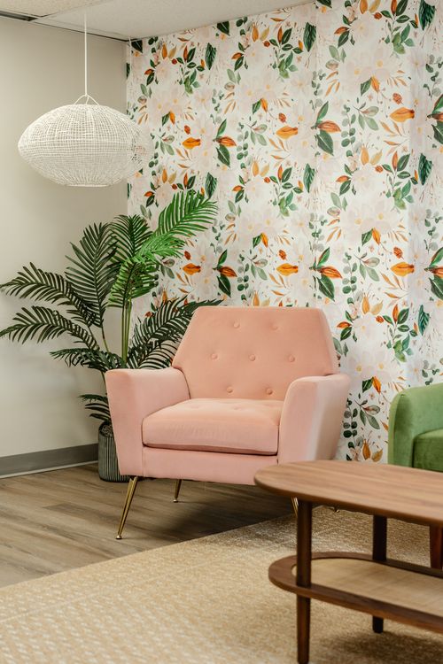 Close-up of a pink tufted armchair beside a potted palm and woven pendant light