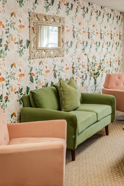 Close-up of a green loveseat and ornate mirror against floral wallpaper