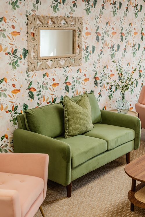 Close-up of a green loveseat, ornate mirror and side table with fresh flowers